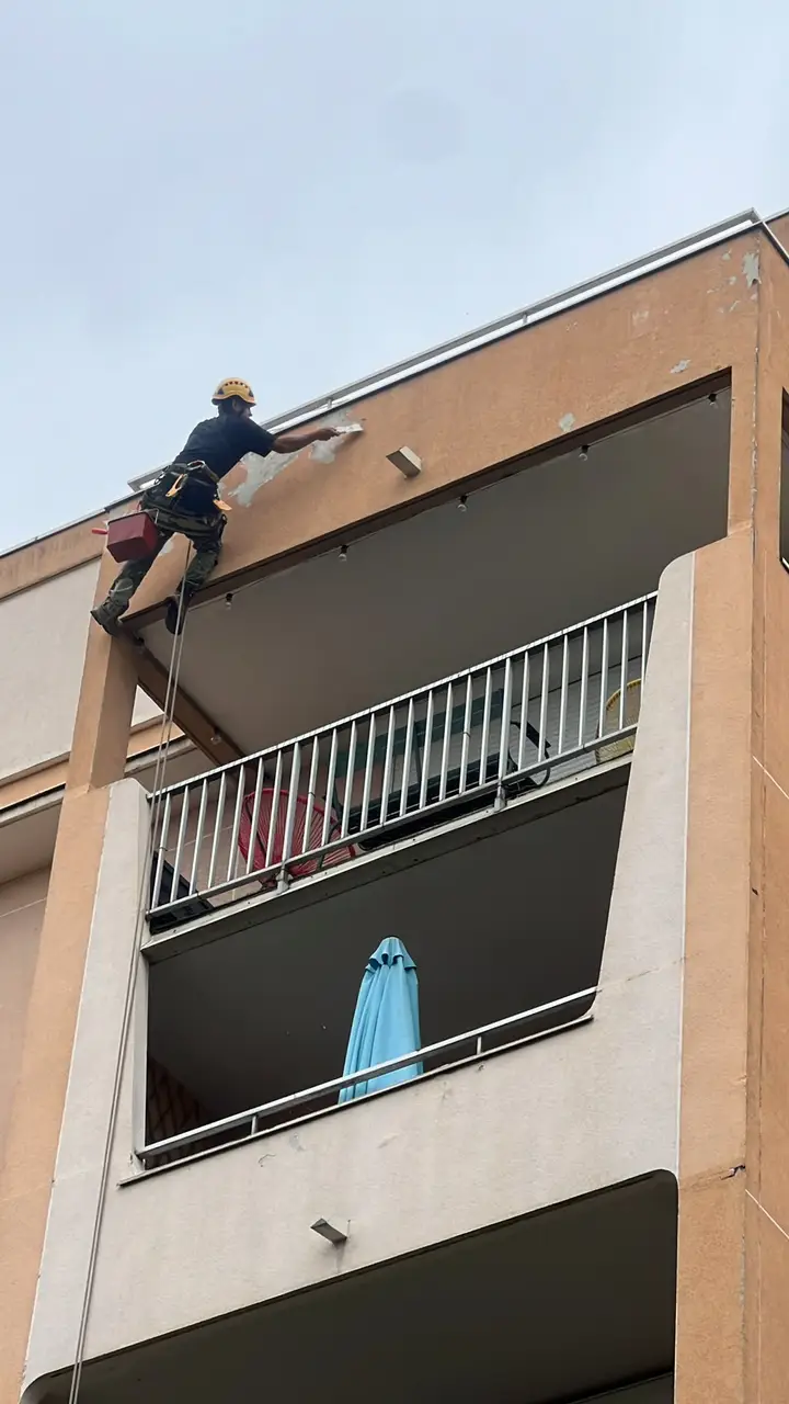 Cordiste au casque jaune, suspendu à sa corde, reprenant l'enduit sous la dalle d'un balcon d'immeuble d'habitation